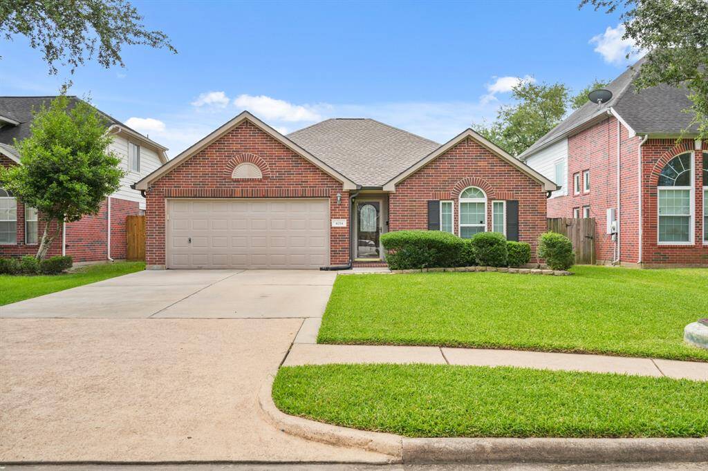 This charming home features a classic red brick exterior with a neatly maintained lawn and landscaping. It includes a two-car garage, arched windows, and a welcoming front entrance, offering great curb appeal in a peaceful neighborhood.