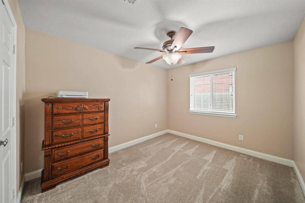 Cozy bedroom with neutral walls and carpet, featuring a ceiling fan and a window for natural light.