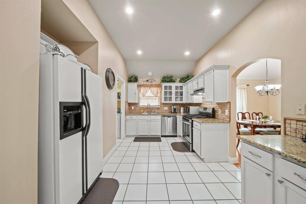 This kitchen features a spacious layout with white cabinetry, stainless steel appliances, and granite countertops. It includes tiled flooring, recessed lighting, and an open archway leading to the dining area, creating a welcoming and functional space.