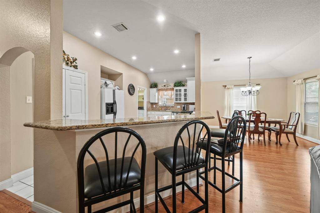 This open-concept space features a kitchen with granite countertops and bar seating, flowing into a bright dining area with hardwood floors and ample natural light from large windows.