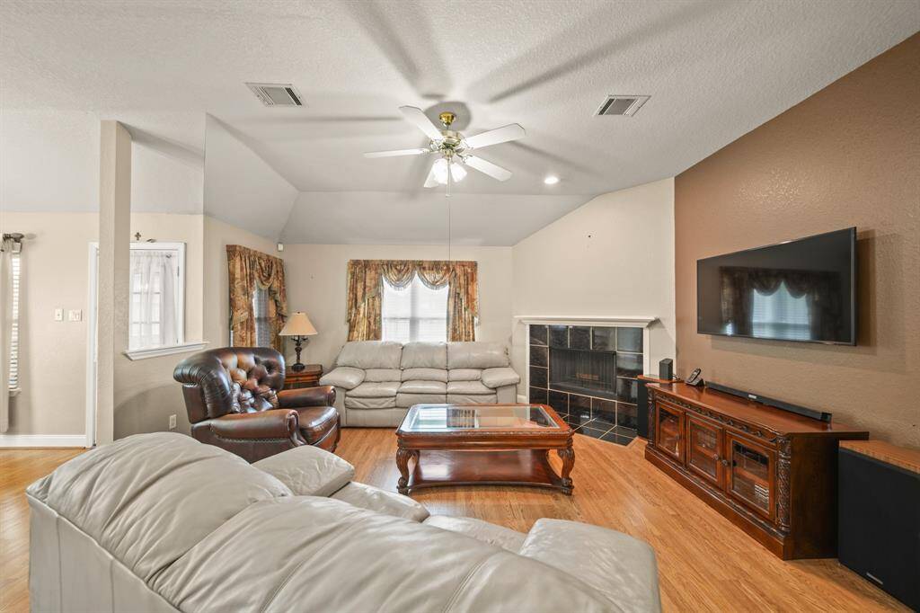This cozy living room features high ceilings, a ceiling fan, and abundant natural light. It includes a comfortable seating area and wood flooring, creating a warm and inviting atmosphere.