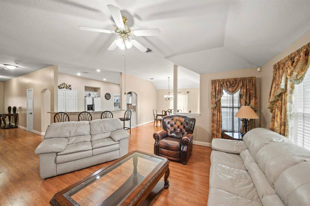 Bright and spacious living area with hardwood floors and neutral walls.  An open layout connects to a kitchen with bar seating and dining area, enhancing the flow of the space.