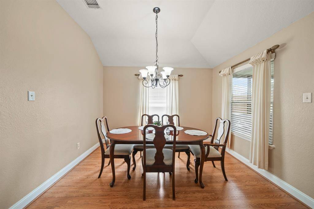Bright dining room with warm wood flooring, a classic chandelier, and large windows featuring elegant drapes. Ideal for family gatherings.