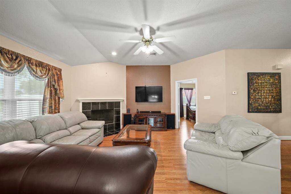 This spacious living room features hardwood floors, a cozy fireplace, and a ceiling fan. It provides a welcoming and comfortable atmosphere.