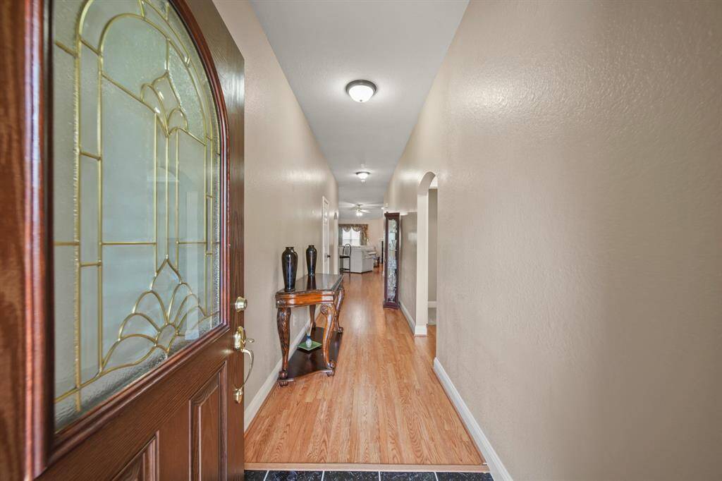 A welcoming entryway with a decorative glass-paneled door. The hallway is long and well-lit, featuring polished wood floors and neutral-toned walls, leading to a bright, spacious area at the end.