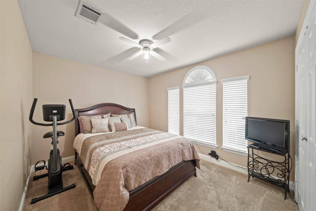 This cozy bedroom features a comfortable bed, neutral walls, and carpeted flooring.  The room is brightened by large windows with blinds, offering plenty of natural light.