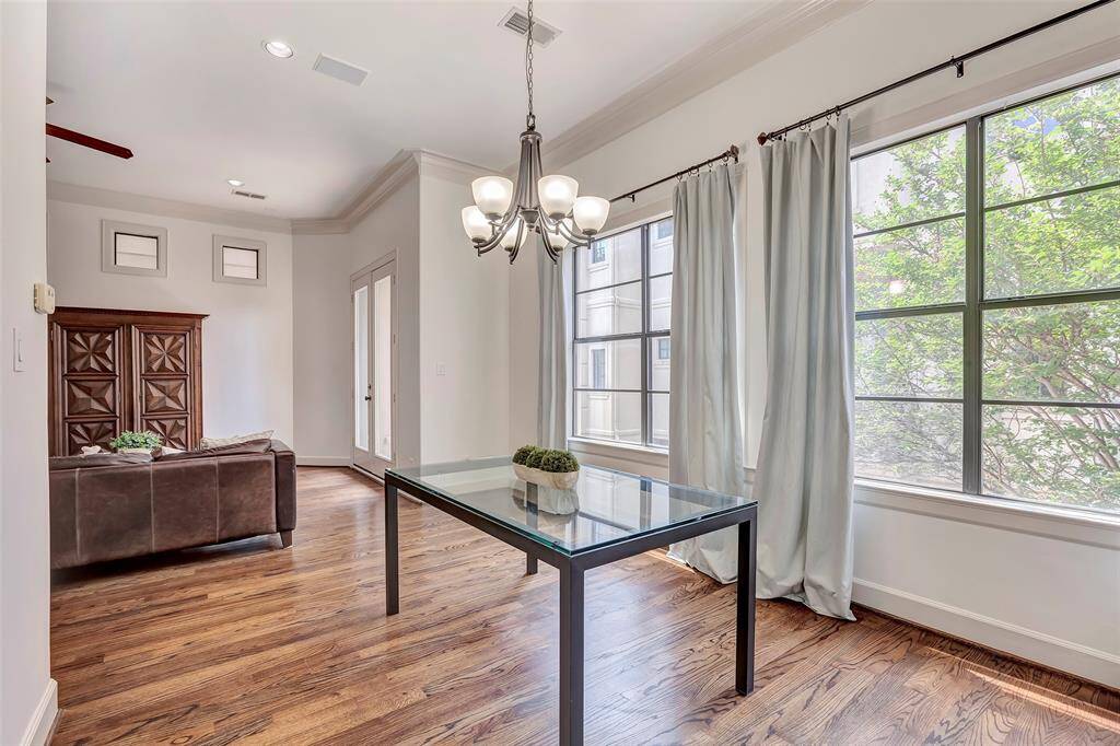 This bright and airy room features large windows with elegant curtains and warm hardwood floors. It seamlessly connects to a cozy living area with a stylish cabinet, creating an inviting space perfect for entertaining or relaxing.