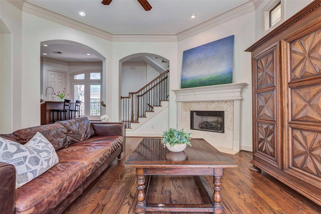 This inviting living room features warm hardwood floors, a cozy fireplace with elegant mantel, and an open layout leading to a staircase. It has access to a kitchen area, perfect for family gatherings.
