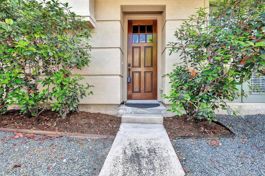 Charming entrance with a wooden door, flanked by lush greenery, leading to a well-maintained walkway. Ideal for a welcoming home feel.