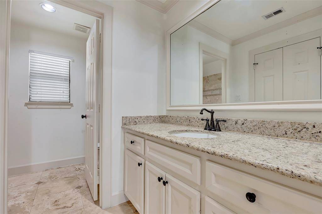 This bathroom features a spacious granite countertop with an undermount sink and dark fixtures. It has a large mirror, white cabinetry, and tiled flooring, offering a clean and modern look.