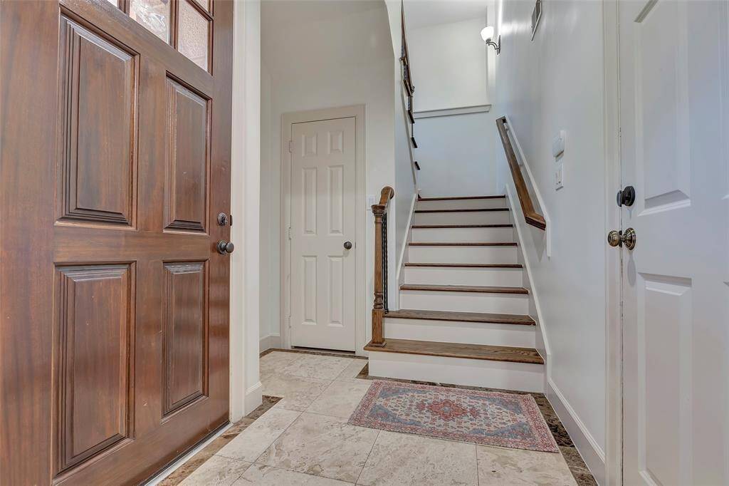 A welcoming entryway with a wooden door, tile flooring, and a staircase with wooden steps and white risers. The space is bright and inviting.