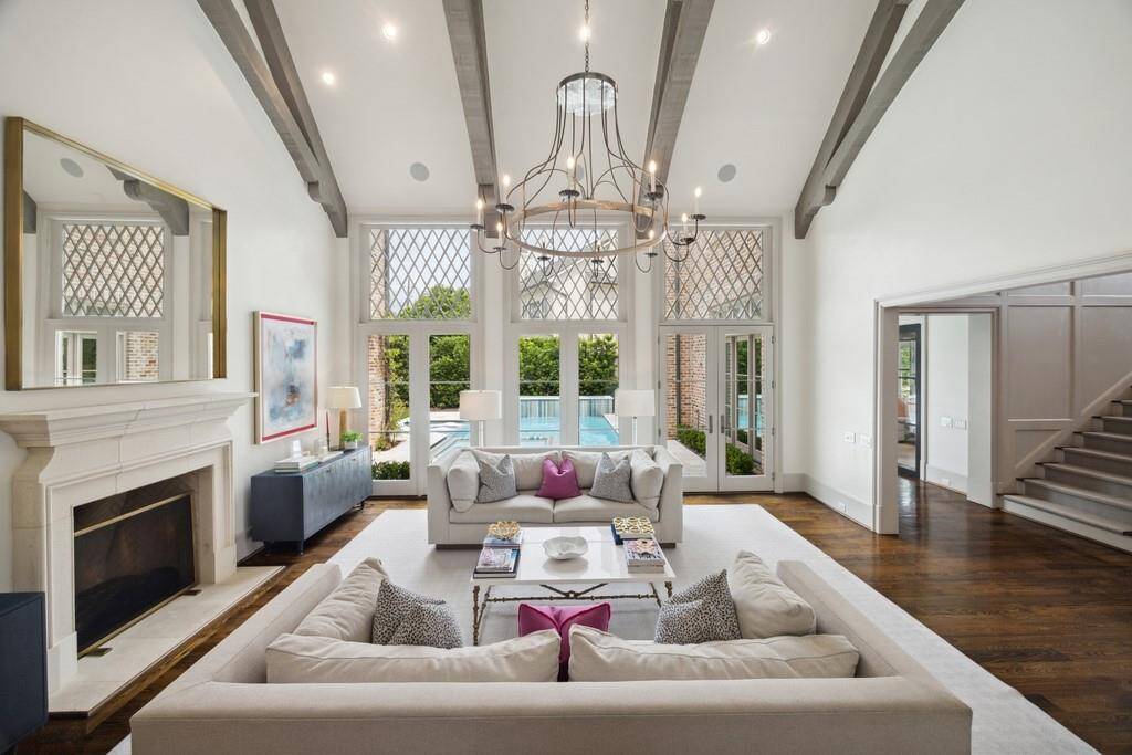 Another view of the living room from the kitchen highlights the stunning symmetry of the space, with double doors leading to the pool, a limestone fireplace, and custom lattice windows that add architectural charm.