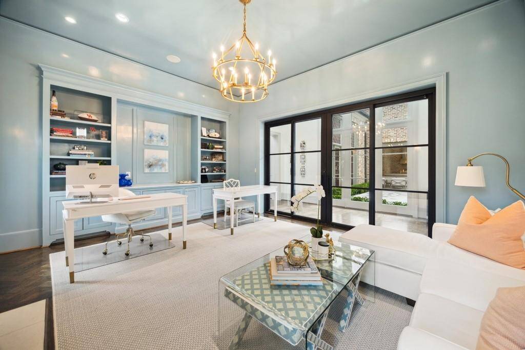 Another view of the office highlights the dramatic steel and glass doors, built-in shelving, and a cohesive high-gloss lacquered finish that elevates the entire space.