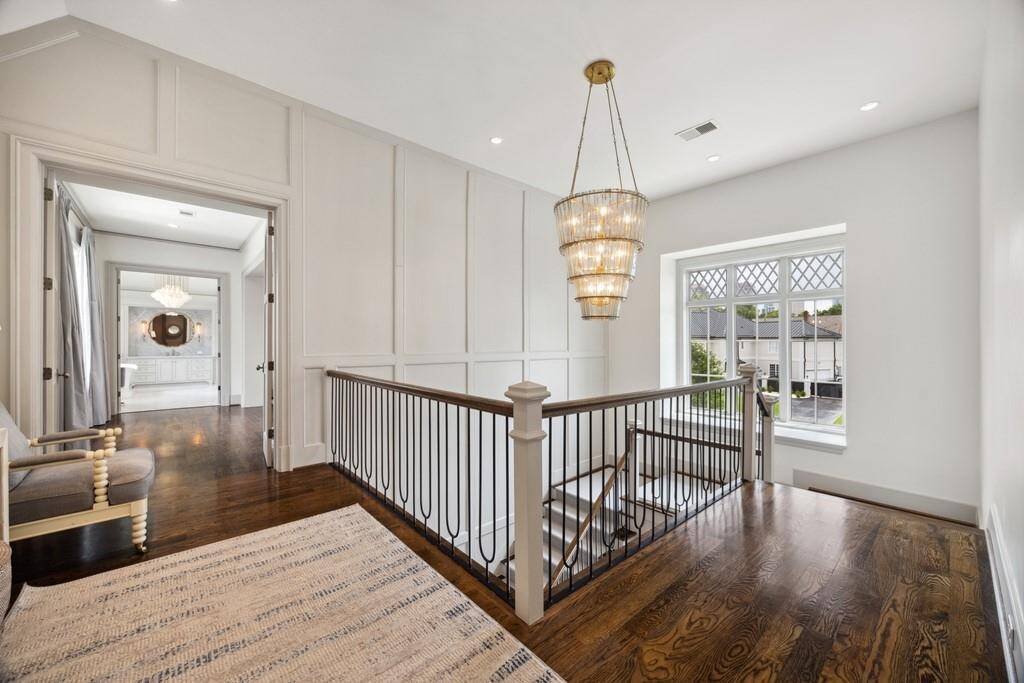 The second-floor landing offers a bright and inviting transition into the primary suite, with a stunning chandelier, elegant wall paneling, and rich hardwood floors. A large window above the staircase fills the space with natural light.