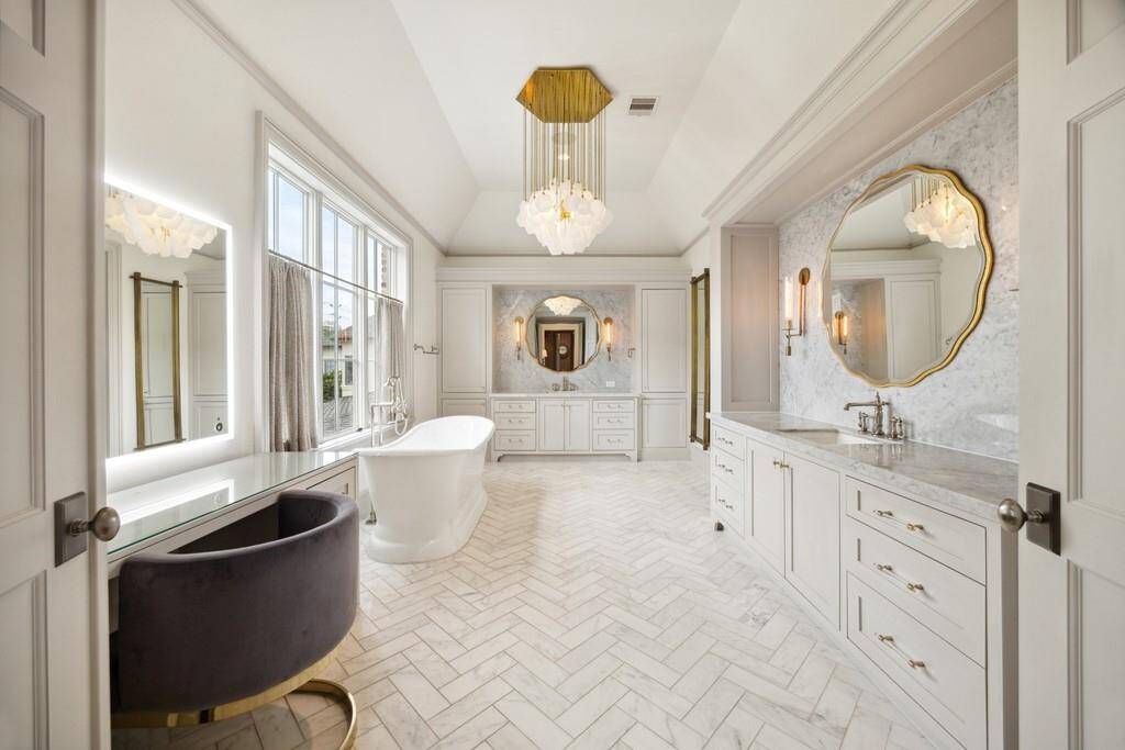 Luxurious bath with herringbone marble floors, soaking tub, dual vanities, and statement lighting.