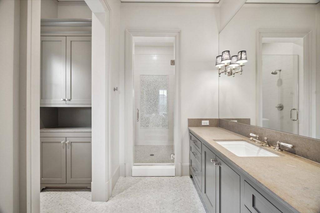 This en-suite bathroom features a spacious walk-in shower with mosaic tile accents, a long quartz vanity with dual sinks, and custom cabinetry for ample storage.