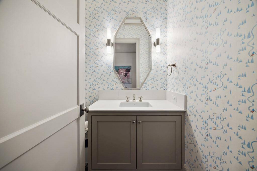 One of four half baths, this playful powder room off the game room features ski-themed wallpaper, a quartz countertop, custom cabinetry, and modern lighting for a fun yet refined finish.