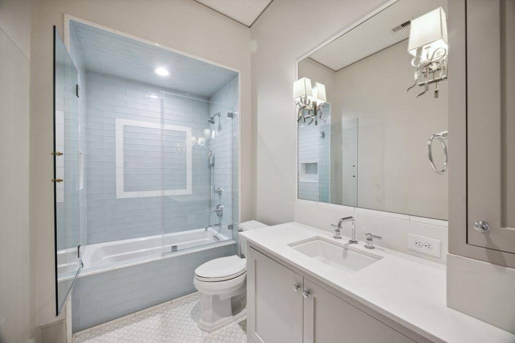 Every bedroom includes an en-suite bath, this one featuring a sleek quartz vanity, polished chrome fixtures, and a tub/shower combo with designer tile surround and frameless glass doors.
