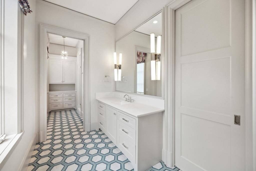 One of five full bathrooms, this space features a bright and fresh design with a crisp white vanity, statement lighting, and playful geometric tile flooring.