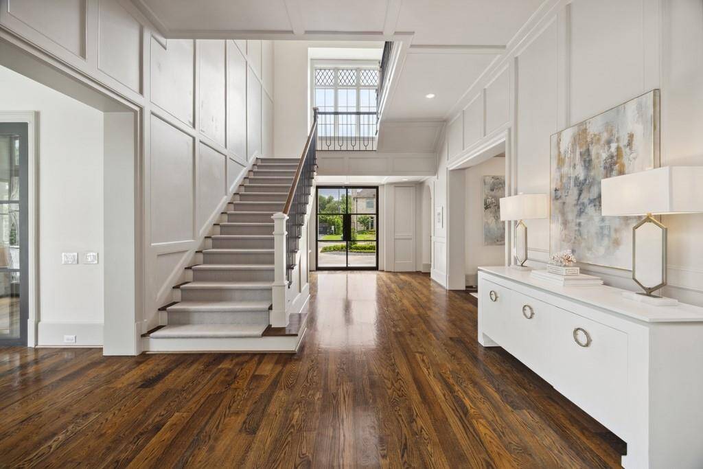 Another view of the entry showcases timeless paneling, soaring ceilings, and a graceful staircase drenched in natural light—an inviting blend of elegance and warmth.