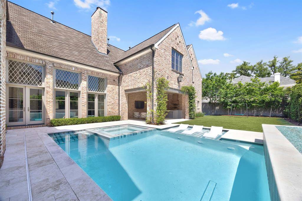 This view captures the full backyard experience—resort-style pool with tanning ledge, a covered outdoor living space with summer kitchen, and an expansive turf yard perfect for play or entertaining.