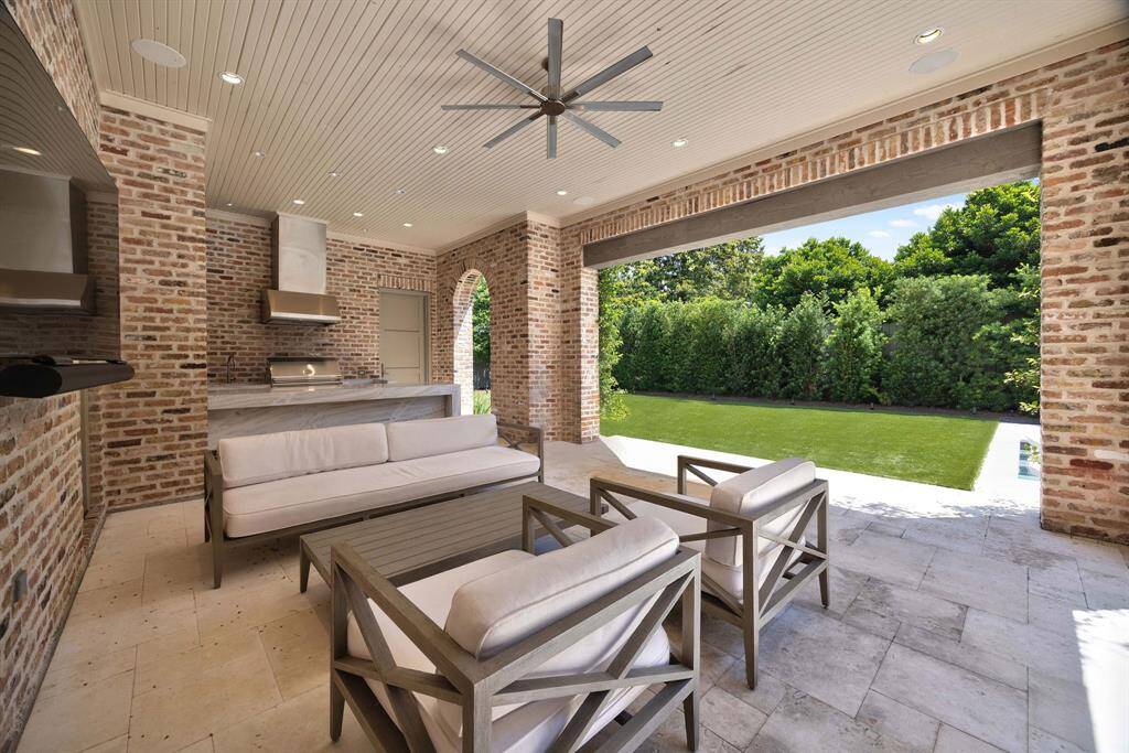 Designed for effortless entertaining, the covered outdoor living area features a full summer kitchen with grill, vent hood, and sleek stone counters—plus a dedicated pool bath discreetly tucked behind the door.