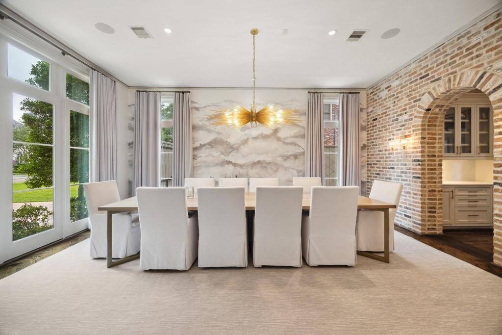 This stunning dining room is a blend of elegance and warmth, featuring floor-to-ceiling windows, a dramatic gold chandelier, and a striking accent wall.