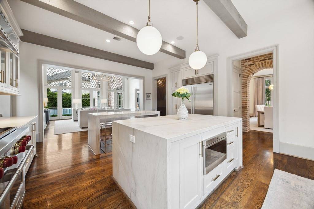 Another view of the kitchen reveals meticulous attention to detail—from the waterfall-edge island and designer pendant lighting to the exposed ceiling beams and custom cabinetry.