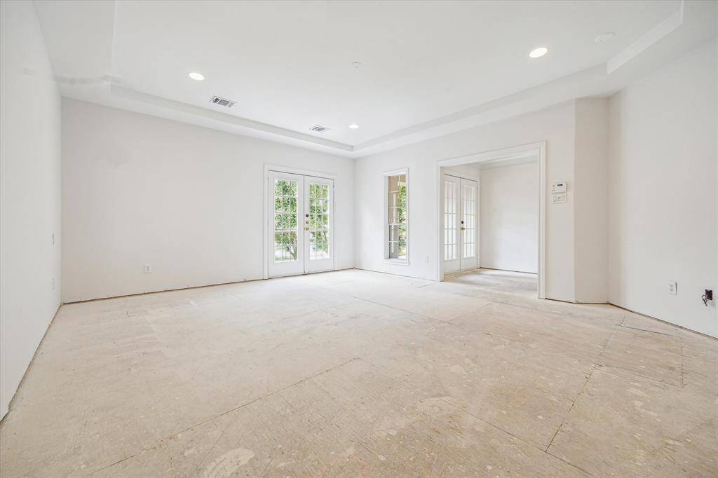 Spacious primary suite with tray ceiling and natural light, featuring French doors that lead to a private balcony overlooking the front yard.