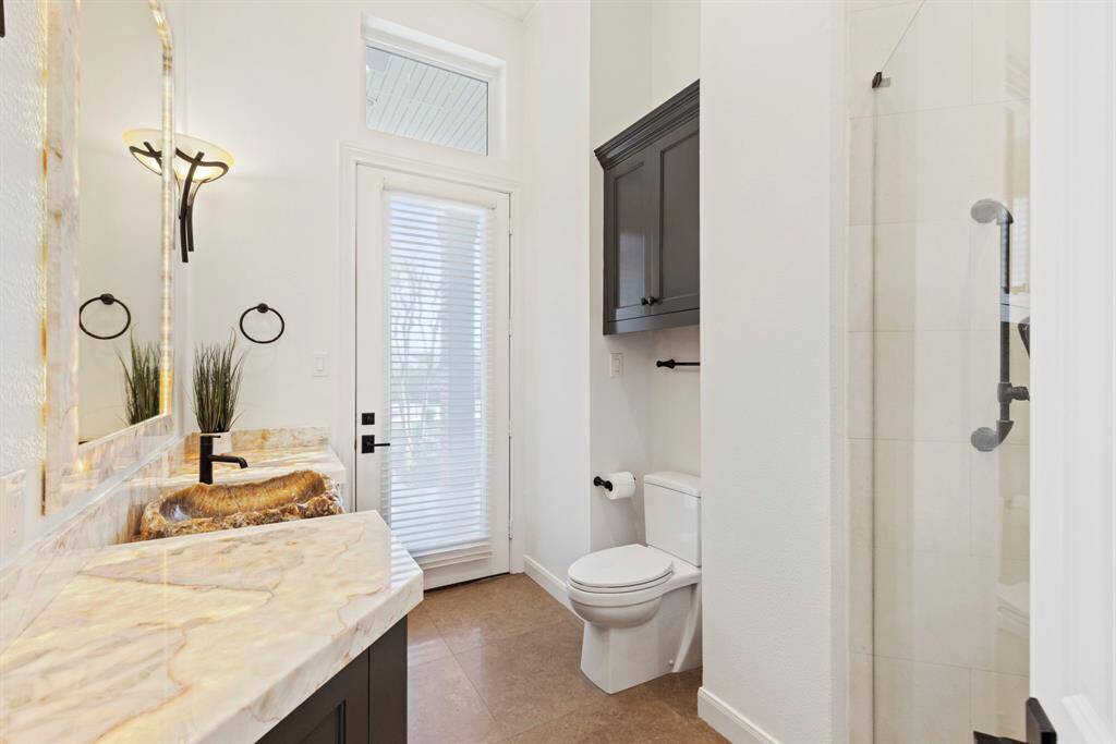 This downstairs  full bath with the quiet opulence of a high-end spa with access to the patio this is the perfect pool bath. A sophisticated blend of natural light and artisan finishes creates a serene ambiance. Convenient outdoor access ensures practicality meets luxury, perfect for that mid-soiree break without missing a beat.