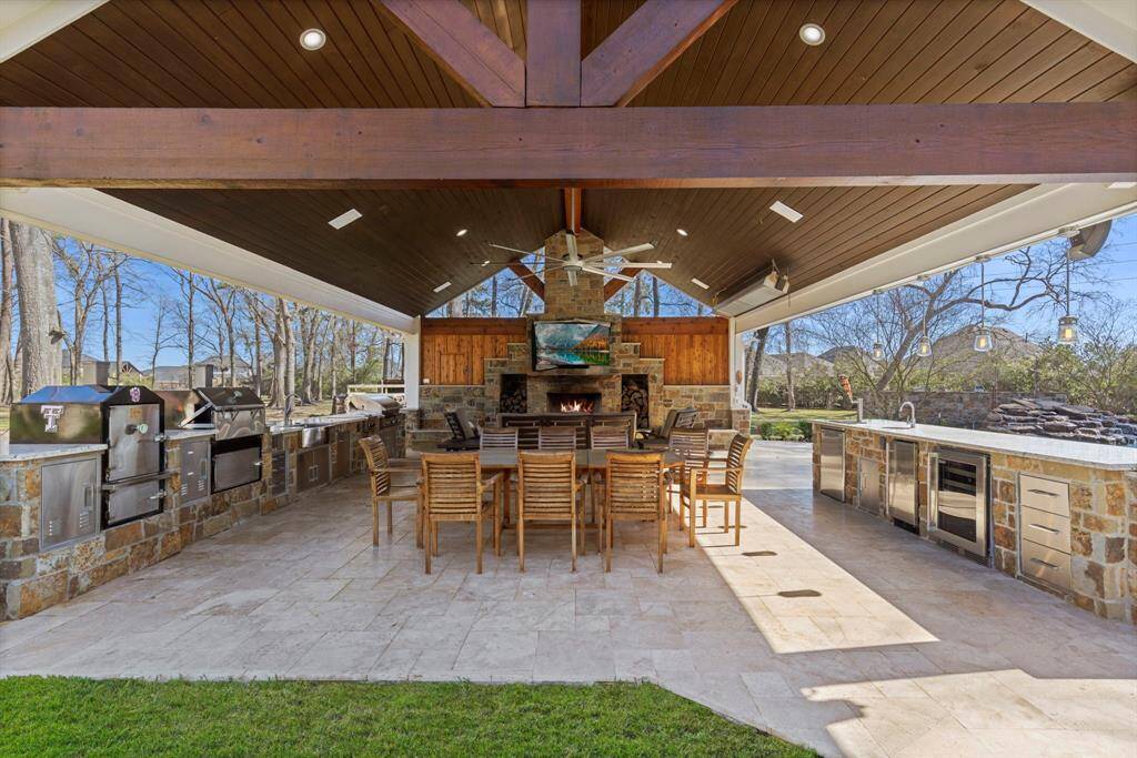 Elevate your entertaining game in this exquisite outdoor kitchen and lounge, where culinary dreams unfold amidst a backdrop of nature's splendor. Imagine sizzling delights on professional-grade grills, while friends gather around the grand stone fireplace. Stay cool under the vaulted timber ceiling, concocting cocktails from the sleek, built-in bar.
