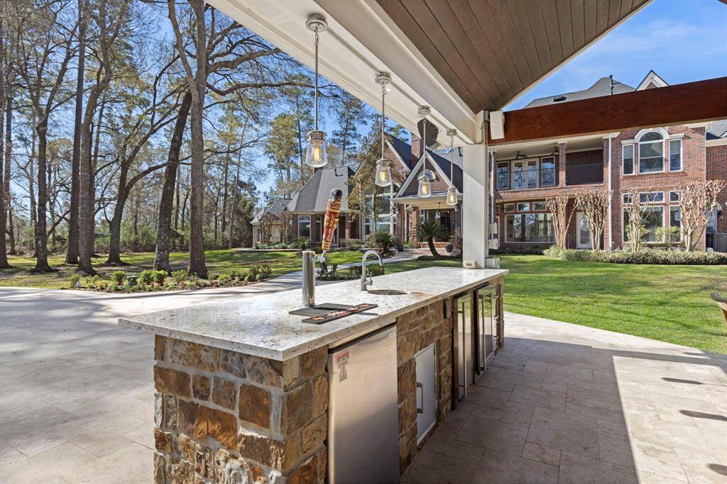Savor the art of outdoor entertaining with this exquisite patio oasis, boasting a stunning stone bar adorned with elegant pendant lighting, keg, ice maker and beverage fridge.