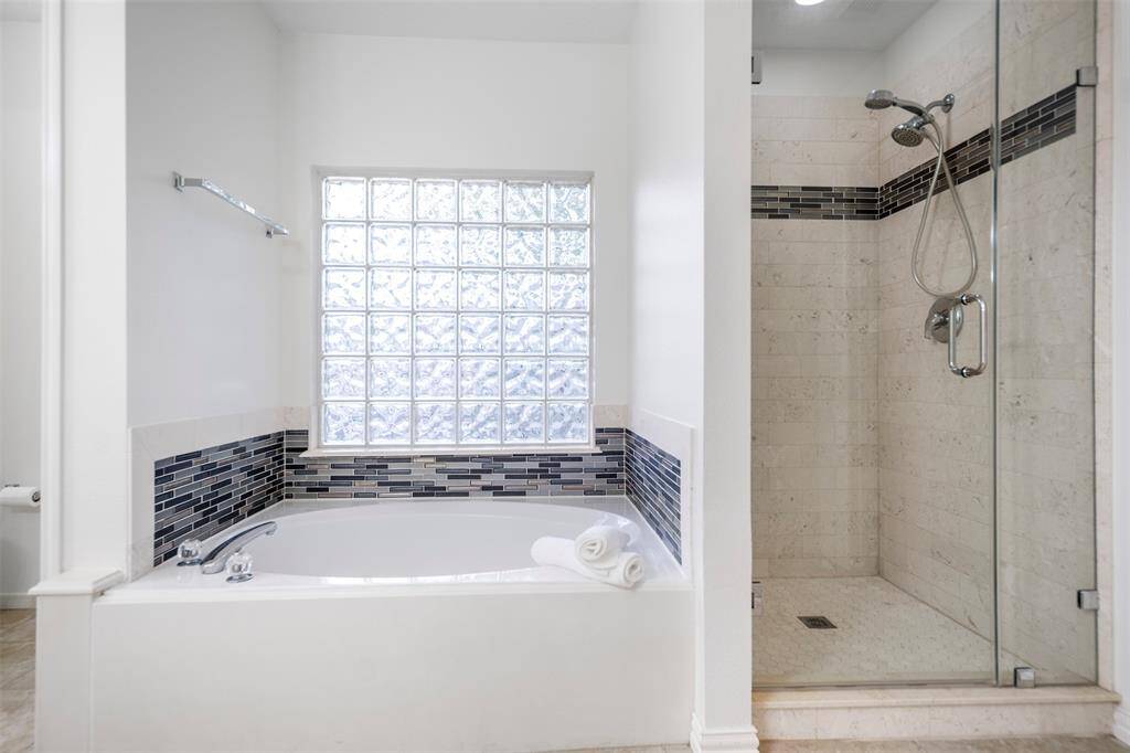 The ensuite bath showcases a luxurious soaking tub, offering a serene space for relaxation. Adjacent to it, the updated shower features sleek, modern finishes, creating a perfect blend of comfort and style in this tranquil retreat.