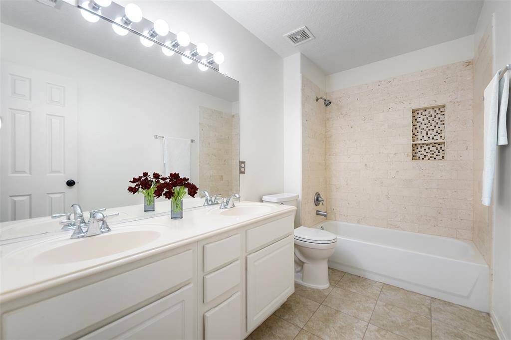The secondary bathroom features an updated shower-tub combo, offering both practicality and style. Dual sinks provide ample space for convenience, while the modern finishes throughout create a clean, refreshed look in this well-appointed space.