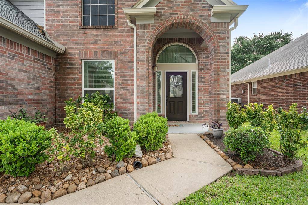 A stunning arched entryway frames the elegant front door, creating a warm and sophisticated welcome. Lush, well-maintained landscaping surrounds the entrance with manicured greenery, enhancing the home's curb appeal.