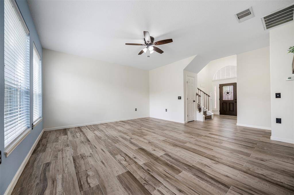 From this angle, the living room highlights its airy, open feel with abundant natural light streaming through the three large windows. The wood-look flooring adds warmth and continuity, creating a welcoming space perfect for relaxing or entertaining.
