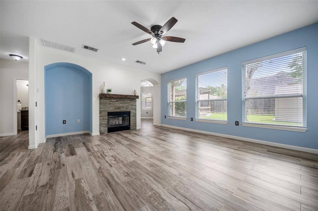 This view of the living room showcases the beautiful stone fireplace with a classic mantle, creating a cozy focal point. Just beside it, an arched wall cut-out adds character and versatility—ideal for an entertainment center, stylish bar cart, or personalized décor display.