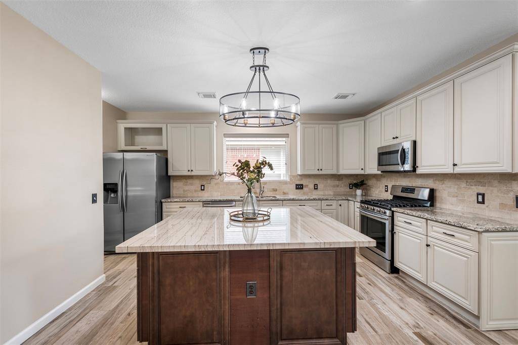 This straight-on view of the kitchen highlights its sleek design, featuring a spacious quartz island at the center, complemented by elegant granite countertops. A modern light fixture illuminates the space, while high-end stainless steel appliances add both style and functionality to this beautifully appointed kitchen.