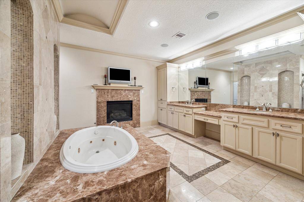 Primary bathroom with double sinks, built in vanity, plenty of overhead lighting, and circular air-jet tub and walk in shower area behind with either side access.