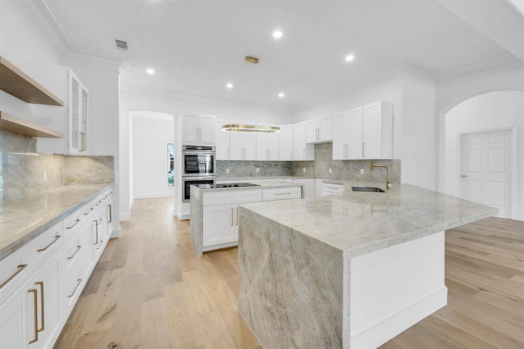A true showstopper, this expansive kitchen features luxurious quartzite countertops, sleek white cabinetry, and gold-tone hardware. The oversized island with waterfall edges and built-in cooktop is perfect for prep, serving, or gathering.