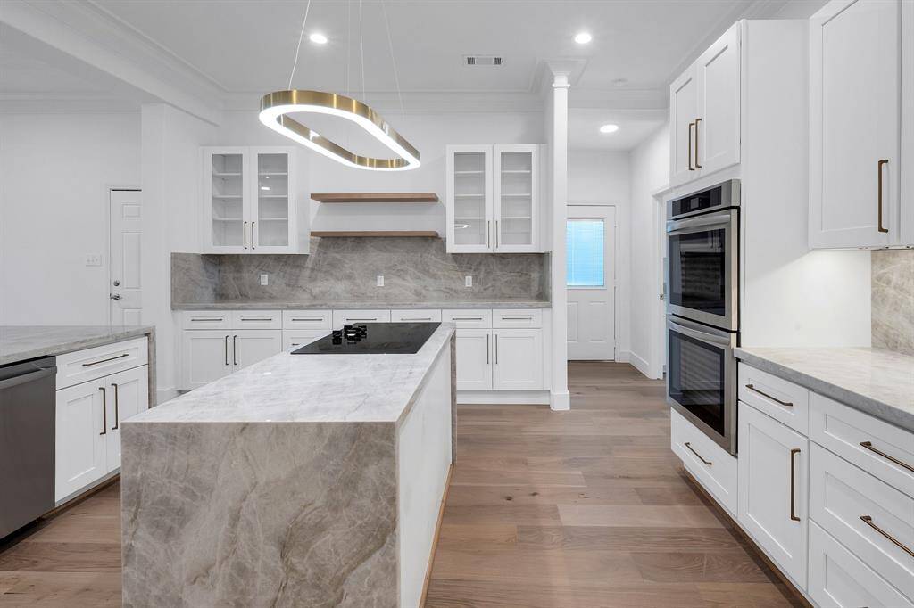 Enjoy double built-in ovens, custom cabinetry with glass inserts, and a sleek cooktop island. Clean lines and a neutral color palette give this kitchen timeless appeal.