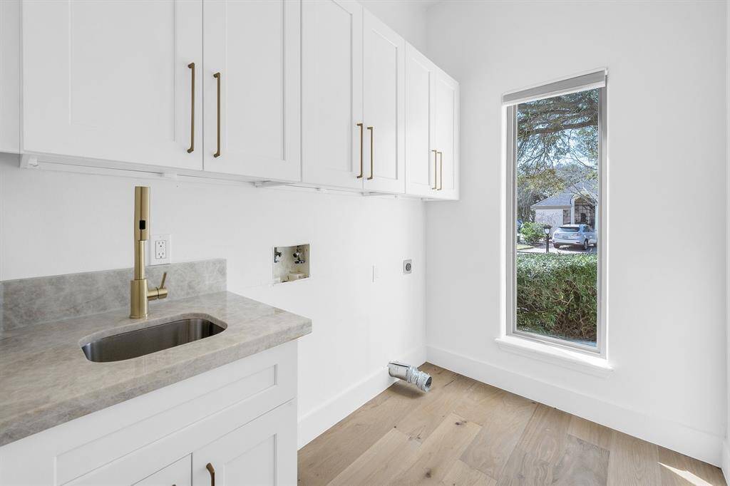 Designed with function and style in mind, the laundry room includes custom cabinetry, quartzite counters, a deep utility sink, and a full-length window that fills the space with natural light.
