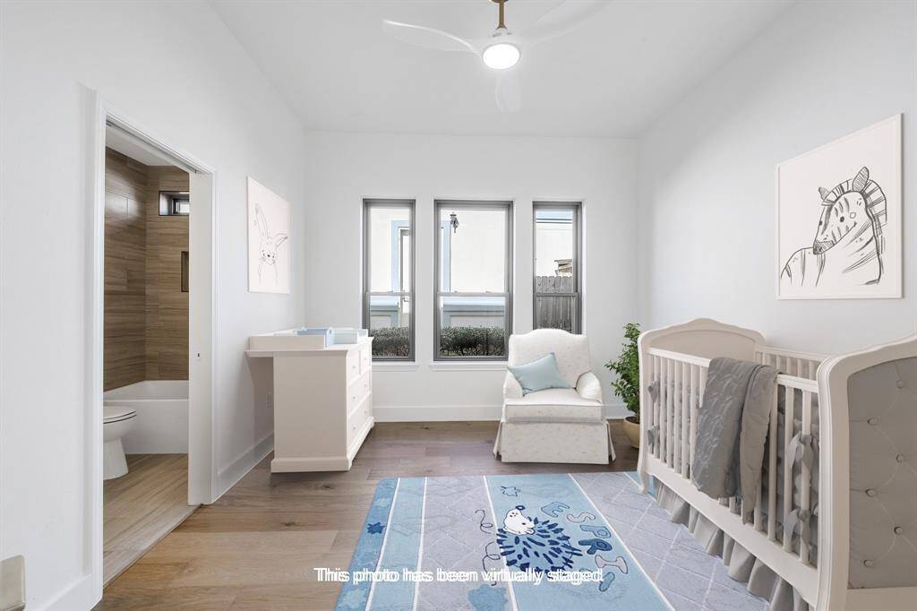 Beautifully staged as a nursery, this downstairs bedroom features soft natural light from three tall windows and direct access to a private full bathroom. Crisp white walls and rich wood floors complete the peaceful setting.