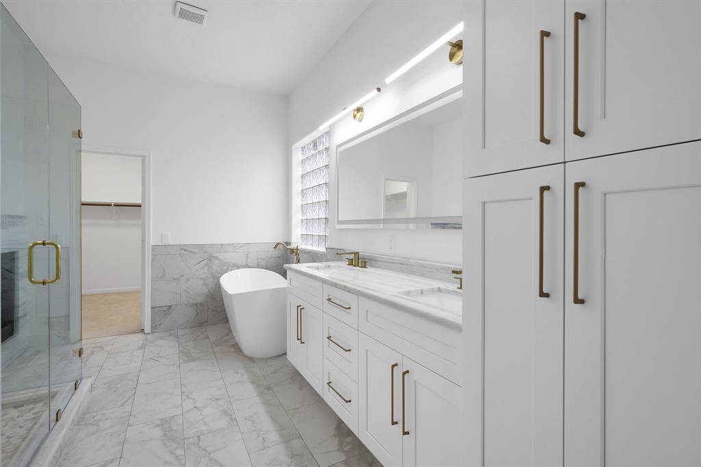 Indulge in spa-like luxury in this fully renovated primary bath, complete with a freestanding soaking tub, walk-in glass shower, dual sinks with dolomite countertops, and stunning brushed gold fixtures. The attached walk-in closet provides abundant space.