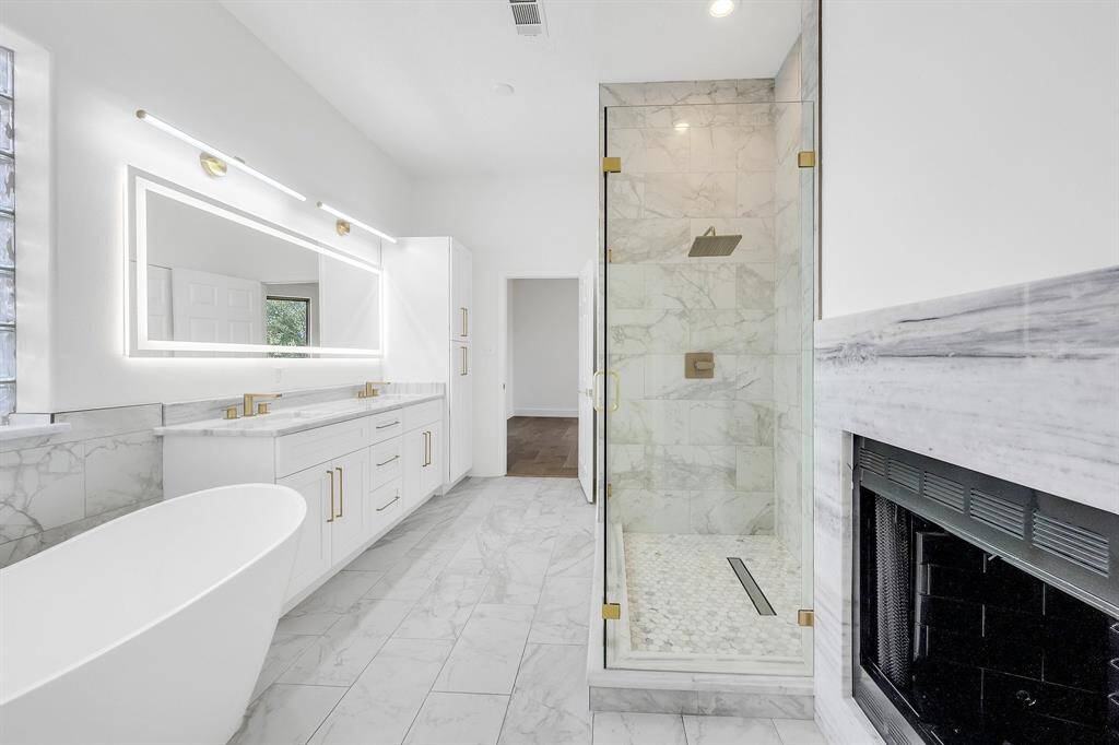 This beautifully updated primary bathroom has a large walk-in shower, rain shower head, and a frameless glass door. The double-sided fireplace adds a unique, cozy touch.