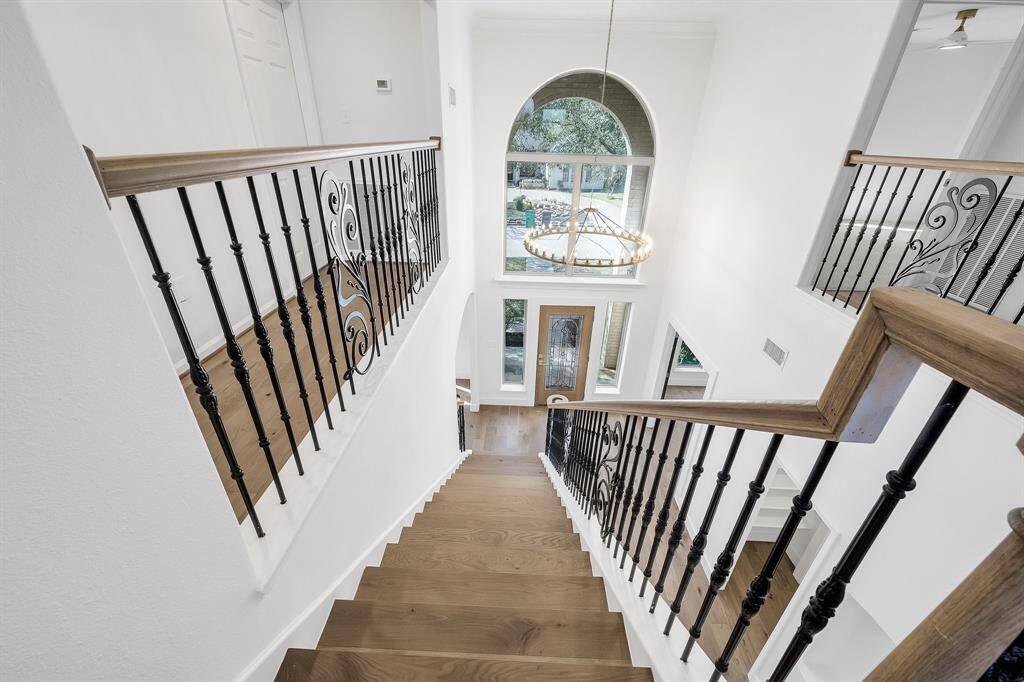 This view from the top of the staircase showcases the stunning two-story foyer with a dramatic arched window, elegant wrought iron and wood railings, and a contemporary chandelier that makes a striking first impression.