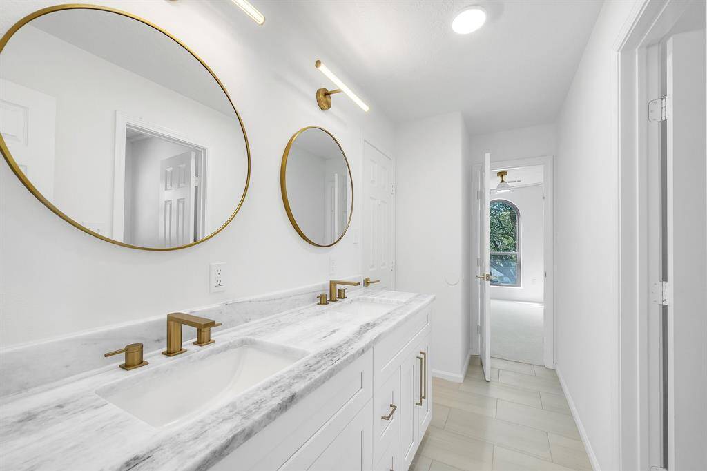 Conveniently located between secondary bedrooms, this stylish Jack-and-Jill bathroom features dual sinks, elegant round mirrors, modern lighting, and brushed gold hardware.