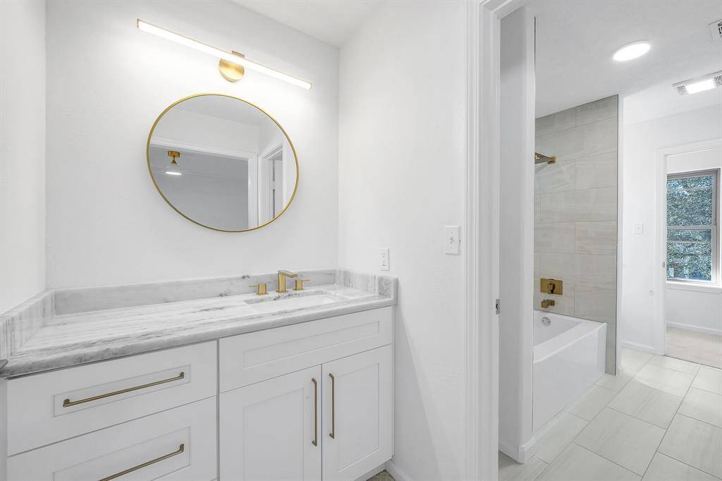 Beautifully updated vanity area with dolomite countertop, brushed gold fixtures, and a modern round mirror, part of the convenient Jack & Jill bathroom layout.