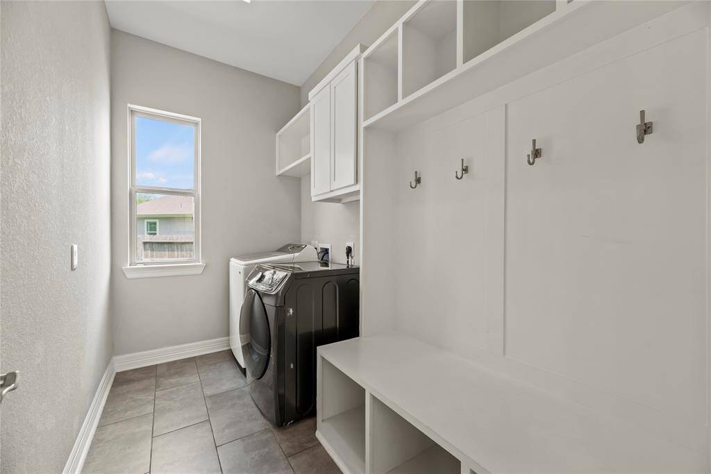 This spacious laundry room features upper cabinet that offer ample storage for cleaning supplies and household essentials. A custom-built mudroom bench with hooks and cubbies provides a stylish and functional space for organizing shoes, bags, and outerwear.