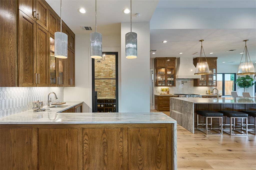 Sophisticated bar featuring a stunning marble tile backsplash, sleek nickel sink, elegant pearl quartzite countertops, and designer Visual Comfort pendant lighting.